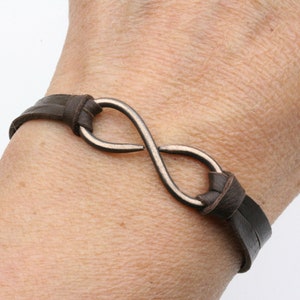 May include: A brown leather bracelet with an infinity symbol charm. The charm is made of silver-toned metal.
