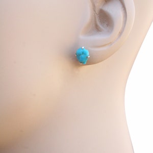 May include: A pair of turquoise stud earrings with silver settings. The earrings are shown on a mannequin's ear.