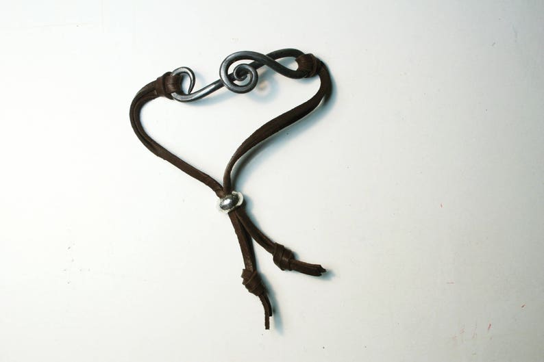 May include: A brown leather bracelet with a silver treble clef charm and a silver bead accent.
