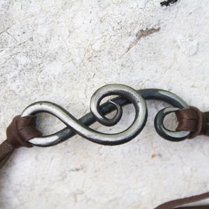 May include: A brown leather cord bracelet with a silver metal infinity symbol charm. The symbol is twisted and has a swirl design.