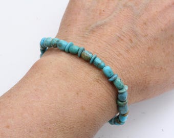 May include: A turquoise beaded bracelet with gold accents. The bracelet is made of small, round beads and is worn on a person's wrist.