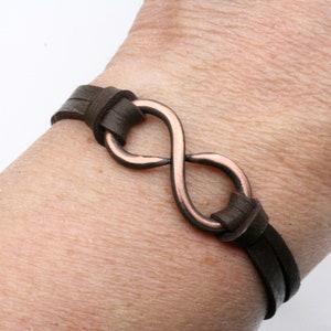 May include: A brown leather bracelet with a copper infinity symbol charm.