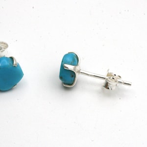 May include: A pair of silver stud earrings with turquoise stones. The stones are a bright blue color and are set in a silver bezel.