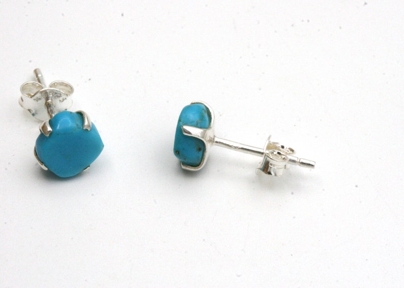 May include: A pair of silver stud earrings with turquoise stones. The stones are a bright blue color and are set in a silver bezel.