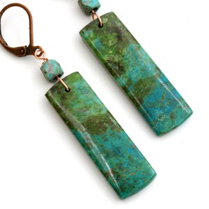 May include: A pair of long, rectangular earrings with a green and blue marbled pattern. The earrings are made with copper wire and have a hook closure.