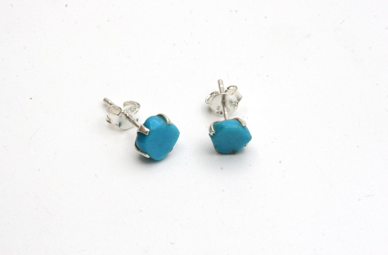 May include: A pair of silver stud earrings with turquoise stones. The stones are a light blue color and have a slightly irregular shape.