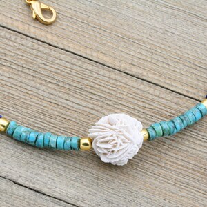 Puede incluir: Un collar de cuentas turquesa, azul y dorado con un colgante de concha blanca.