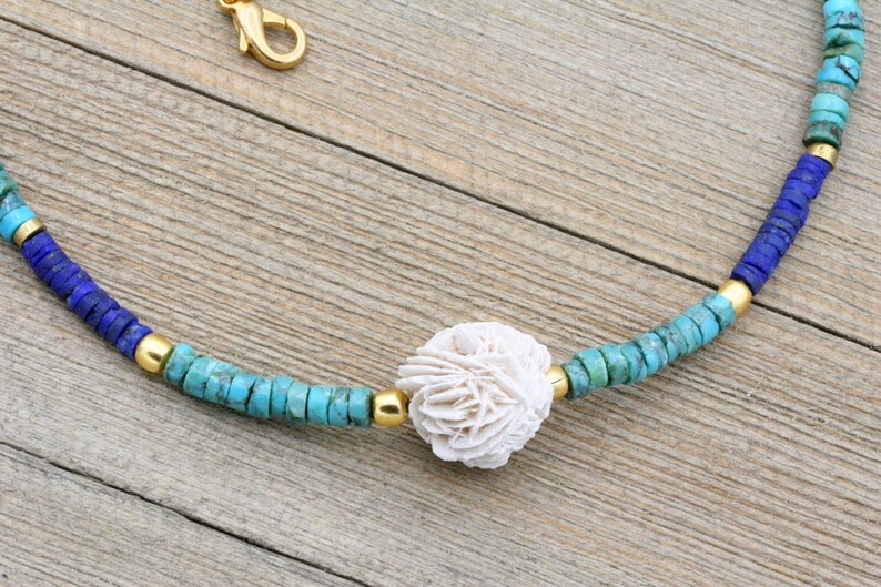 Puede incluir: Un collar de cuentas turquesa, azul y dorado con un colgante de concha blanca.
