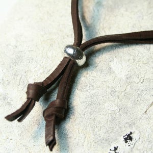 May include: A brown leather cord necklace with a silver metal bead accent. The cord is tied in a knot at the end.