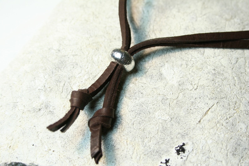 May include: A brown leather cord necklace with a silver metal bead accent. The cord is tied in a knot at the end.