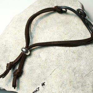 May include: A brown leather bracelet with a silver bead and a metal clasp. The bracelet is on a white surface.