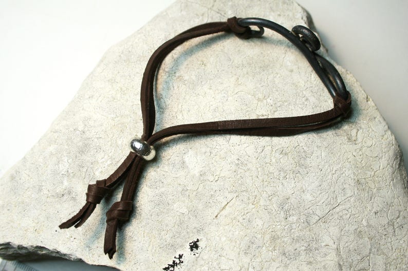May include: A brown leather bracelet with a silver bead and a metal clasp. The bracelet is on a white surface.