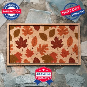 May include: A brown coir doormat with a pattern of colorful autumn leaves. The doormat has a beige background with a repeating pattern of red, orange, and brown leaves.