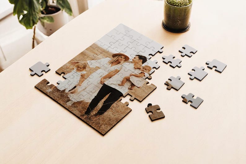 May include: A personalized family photo puzzle with pieces scattered on a light wood surface. The puzzle features a family portrait with a couple and two children. Several gray puzzle pieces are scattered around the partially assembled puzzle.
