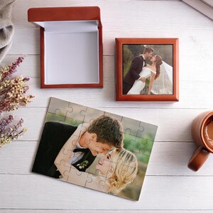 May include: A wedding-themed still life featuring a framed photo, a jigsaw puzzle, and a gift box, all with images of a couple. A mug of coffee and dried flowers are also present. The items are arranged on a white wooden surface.