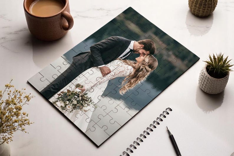 May include: A completed jigsaw puzzle featuring a romantic image of a couple embracing. The puzzle shows a man in a suit and a woman in a wedding dress. The puzzle is on a white surface with a cup of coffee and a plant.