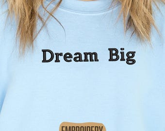 Könnte beinhalten: Hellblaues Sweatshirt mit dem gestickten Text "Dream Big" in Schwarz. Das Wort "EMBROIDERY" ist in einem braunen Rechteck unten gestickt. Das Sweatshirt ist einfarbig und hat einen Rundhalsausschnitt.