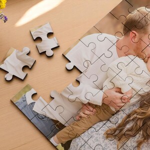 May include: A custom photo puzzle featuring a family embracing. The puzzle pieces show a man kissing a child, with a woman nearby. The puzzle is on a light wood surface, with a vase of flowers.