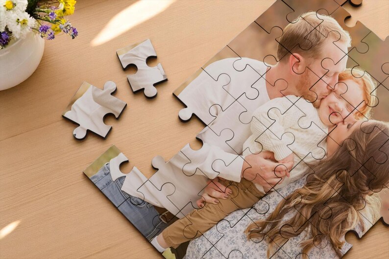 May include: A custom photo puzzle featuring a family embracing. The puzzle pieces show a man kissing a child, with a woman nearby. The puzzle is on a light wood surface, with a vase of flowers.