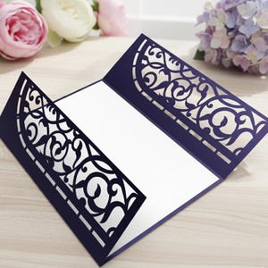 May include: Navy blue invitation card with intricate, laser-cut floral design. The card is open, revealing a blank white interior for personalized text. The design is a decorative element for weddings, parties, or special events.