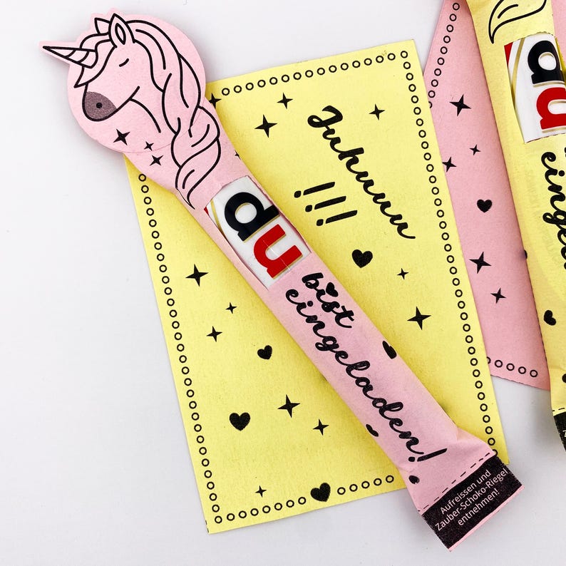 May include: A pink and yellow card with the text "Juhuuu!!! du bist eingeladen!" and a pink chocolate bar with a unicorn design and the text "du" on it.