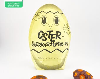 May include: A yellow paper Easter egg craft with a chick face and the text "OSTER-ÜBERRASCHUNGS-Ei" for a surprise egg. Two chocolate eggs with orange and brown designs are in the foreground.