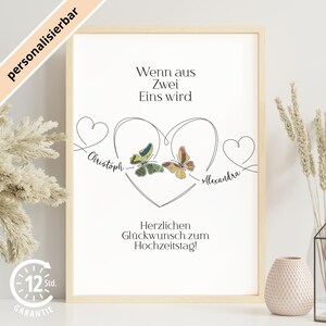 Pode incluir: Uma impressão emoldurada com o texto "Wenn aus Zwei Eins wird" e "Herzlichen Glückwunsch zum Hochzeitstag!". A obra de arte apresenta um design em forma de coração com borboletas e os nomes "Christoph" e "Alexandra".