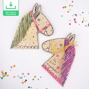 Op de afbeelding: Twee bruine papieren paard-kop uitsnijdingen met gele en roze manen en staarten. Het paard rechts heeft de tekst "Du bist eingeladen!" erop geschreven.