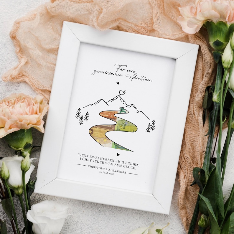 Personalisiertes Bild für das Brautpaar auf der eine Zeichnung einer Landschaft mit Fluss und Bergen zu sehen ist. Der Fluss ist ausgeschnitten, dahinter sind Geldscheine befestigt – ein kreatives Geldgeschenk zur Hochzeit. Darunter ist das Bild personalisiert mit Namen und Datum der Hochzeit. Die Druckvorlage ist die perfekte Last Minute Geschenk Idee – schnell gebastelt und einzigartig!