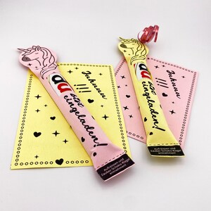 May include: Two pink and yellow unicorn-shaped chocolate bar wrappers with the text "Juhunu!!!  bitte eingeladen!"  The wrappers are decorated with stars and hearts.