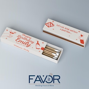 May include: Two white matchboxes with red text and illustrations. One box reads "Happy Birthday Emily" with a date and location. The other box says "Let's eat, drink and have a good time." Matches are visible.