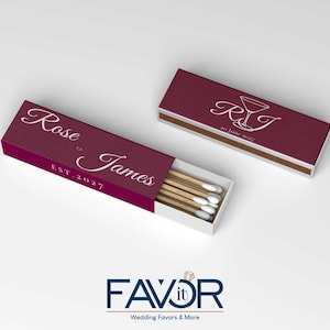 May include: Burgundy matchboxes with custom text. One box is open, revealing matches. The text on the boxes reads "Rose & James EST. 2027" and "RJ 20 June 2027" with a cocktail glass graphic. Wedding favors.