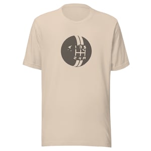 May include: A beige t-shirt featuring a brown graphic of a car's gear shift pattern. The pattern includes the numbers 1, 2, 3, 4, 5, and R.