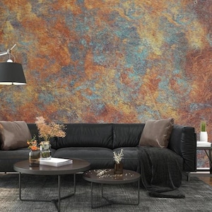 Könnte beinhalten: Ein schwarzes Ledersofa mit zwei Kissen und einer Decke vor einer Wand mit einer rostigen, strukturierten Tapete. Zwei Couchtische mit schwarzen Metallrahmen und dunklen Holzplatten stehen vor dem Sofa.