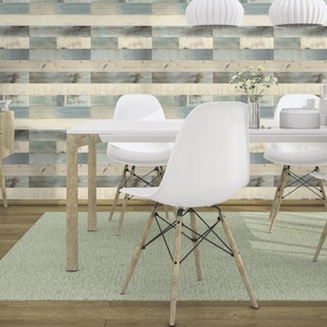 Pode incluir: Uma mesa de jantar branca com quatro cadeiras brancas e um tapete verde claro. A mesa e as cadeiras têm pernas de madeira. A parede atrás da mesa é coberta com um papel de parede de aparência de madeira em um esquema de cores azul claro e marrom.