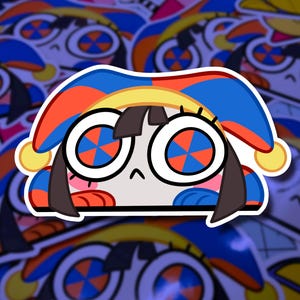 Puede incluir: Una pegatina que representa un personaje de dibujos animados con ojos grandes y una expresión triste. El personaje lleva un sombrero con detalles azules, naranjas y amarillos. La pegatina tiene un borde blanco y está sobre un fondo de pegatinas similares.
