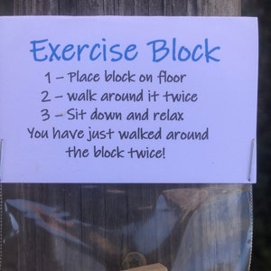May include: A white card with blue text that reads "Exercise Block" and instructions on how to use a wooden block for exercise. The card is in a clear plastic bag with a small wooden block inside.