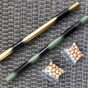 May include: Two wooden dowels, one painted gold and the other with a black and green camouflage pattern. Two small bags of chickpeas are in the foreground.