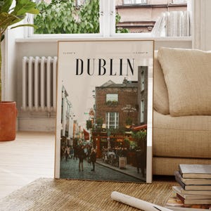 May include: A framed print featuring a street scene in Dublin, Ireland, with the city name in large black letters at the top. The image shows a cobblestone street with buildings, people, and the Temple Bar pub.