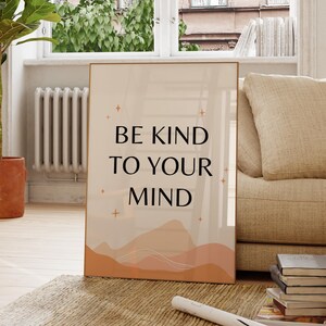May include: A framed print with the text "BE KIND TO YOUR MIND" in black against a beige background. The print features a minimalist landscape design in shades of orange and peach. Decorative stars are scattered around the text.