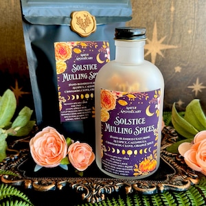 May include: A black pouch with a gold wax seal and a frosted glass bottle, both featuring purple labels with floral designs and the text Solstice Mulling Spices. The labels list ingredients including allspice, calendula, cinnamon, clove, and orange spice.