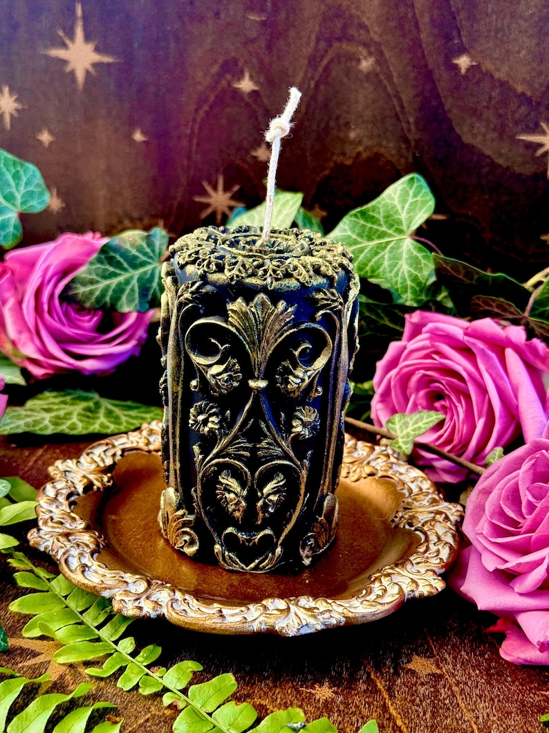 May include: A black and gold decorative candle with an ornate design. The candle is sitting on a gold-colored plate.