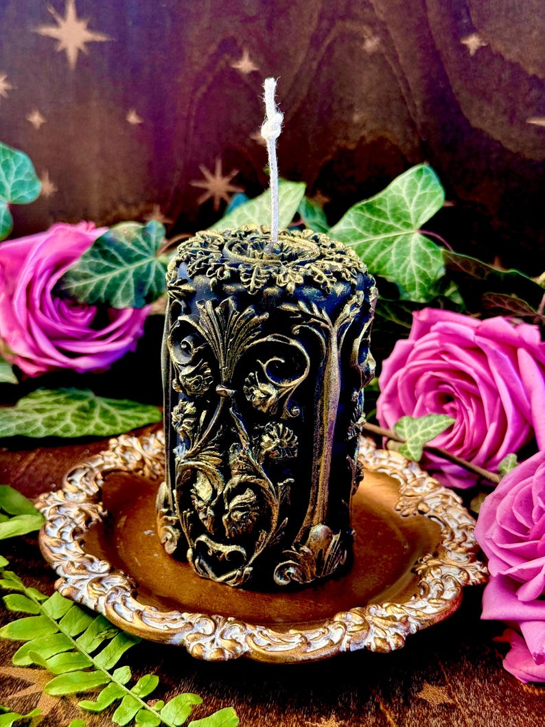 May include: A black and gold candle with an ornate design. The candle is sitting on a gold tray.
