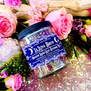 May include: A glass jar filled with a blend of dried herbs and flowers, labeled "La Luna Brew Organic Loose-Leaf Evening Tea". The label lists ingredients including peppermint, ginger, lavender, orange peel, fennel, lemon balm, chamomile, rose petals, and papaya leaf.