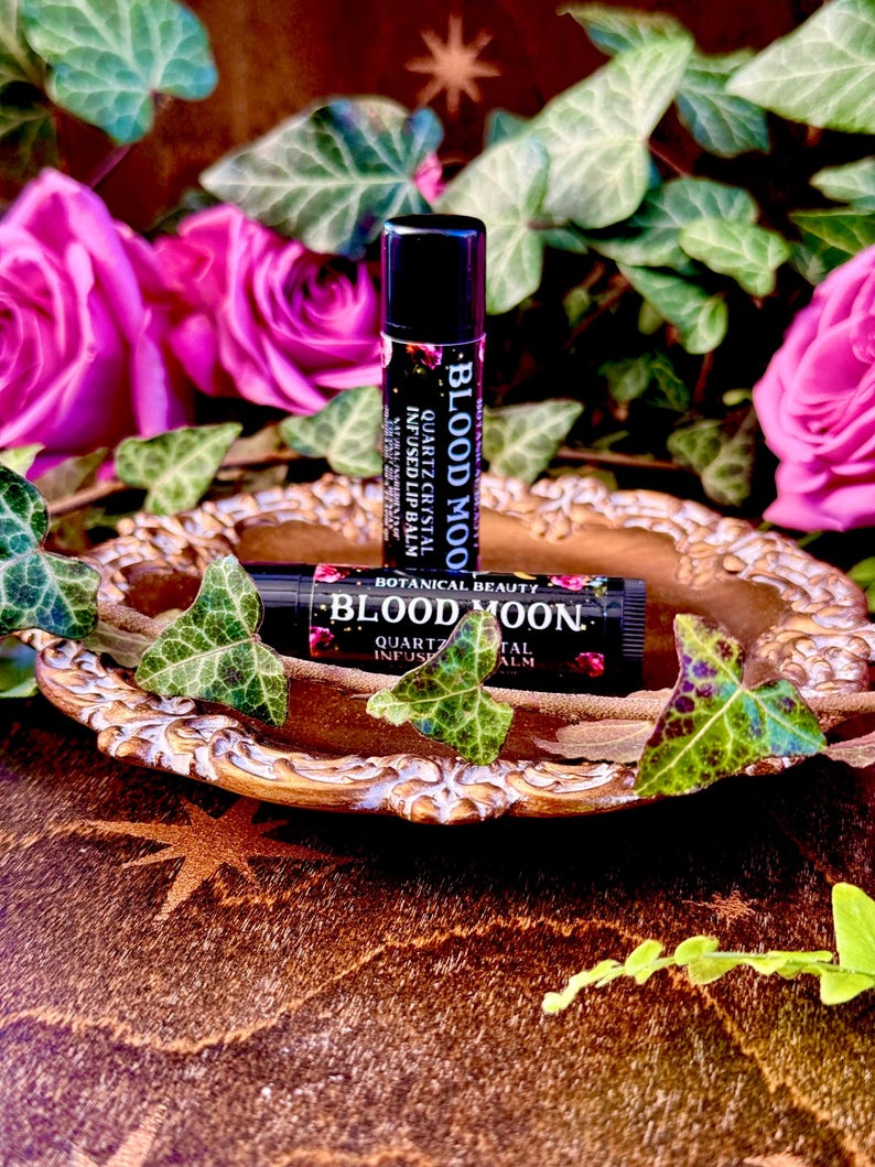 May include: Two tubes of lip balm with the words "Blood Moon" and "Quartz Crystal Infused Lip Balm" on the labels. The tubes are on a gold-colored tray with a star design.