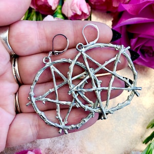 May include: Silver earrings with a pentagram design made of twisted branches. The earrings are dangling and have a hook closure.