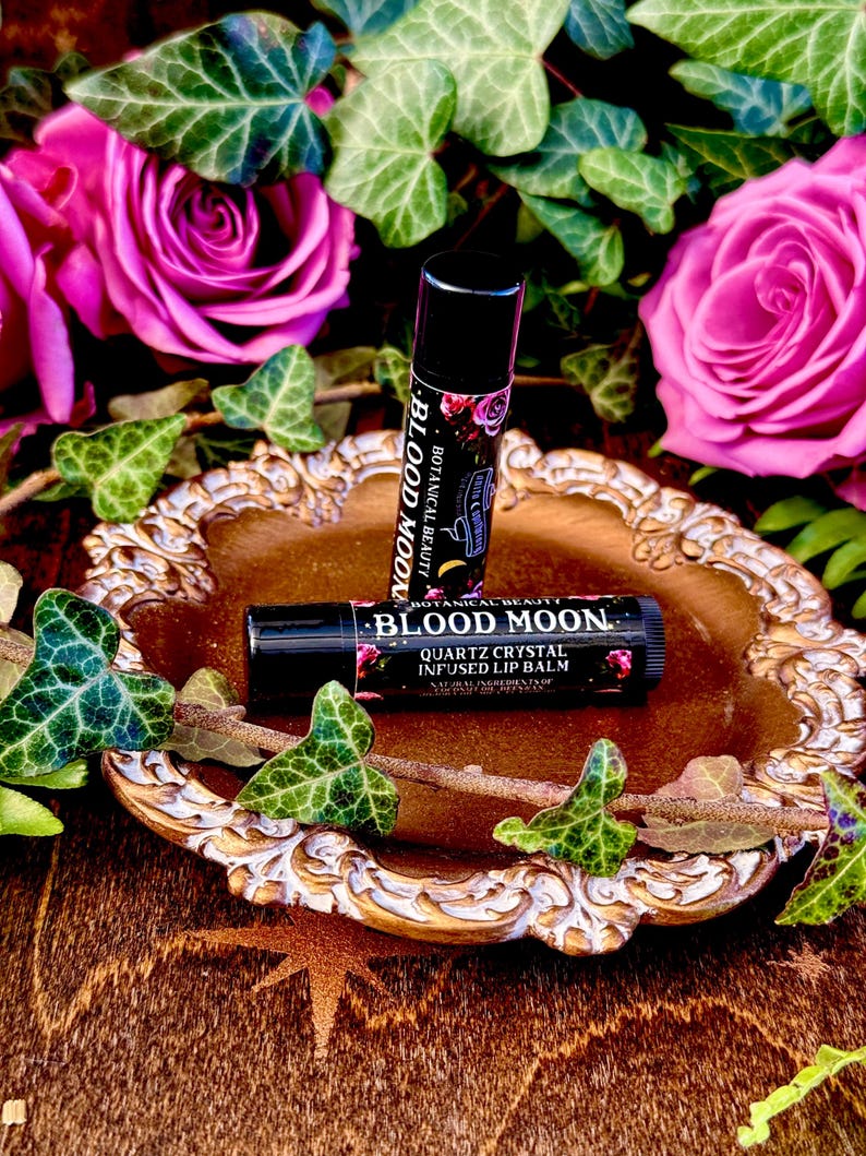 May include: Two black tubes of Blood Moon Quartz Crystal Infused Lip Balm on a gold decorative tray with pink roses and green ivy.