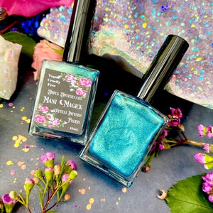 May include: Two bottles of teal nail polish with black caps. The bottles are labeled "Anita Apothecary Mani C Magick Crystal Infused Polish" with a floral design. The background includes flowers and crystals.