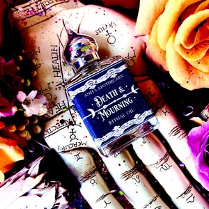 Pu&ograve; includere: Un piccolo flacone di vetro blu scuro con un tappo argentato e un'etichetta che recita "Anita Apothecary Death & Mourning Ritual Oil". Il flacone &egrave; tenuto in una mano con uno sfondo bianco che presenta simboli e segni astrologici.