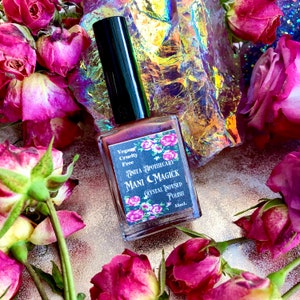 May include: A bottle of Mani Magick crystal-infused polish by Anita Apothecary, surrounded by dried pink roses. The label reads "Vegan, Cruelty Free" and features floral accents. The nail polish bottle has a black cap and contains 15ml of product.